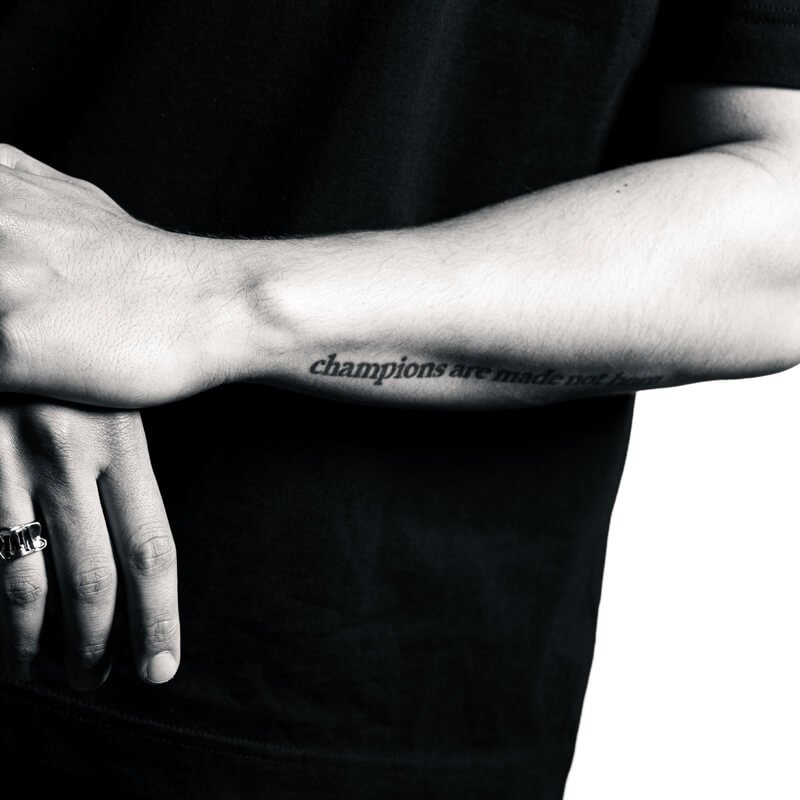 Close-up of a forearm tattoo reading 'champions are made not born'